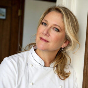 Chef Sara smiling in the kitchen, wearing a professional apron while preparing a delicious Passover Potato Pie.